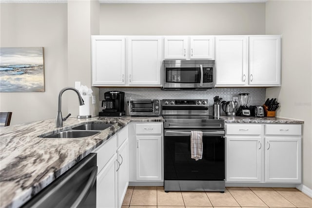 kitchen with sink, light stone counters, light tile patterned flooring, white cabinets, and appliances with stainless steel finishes