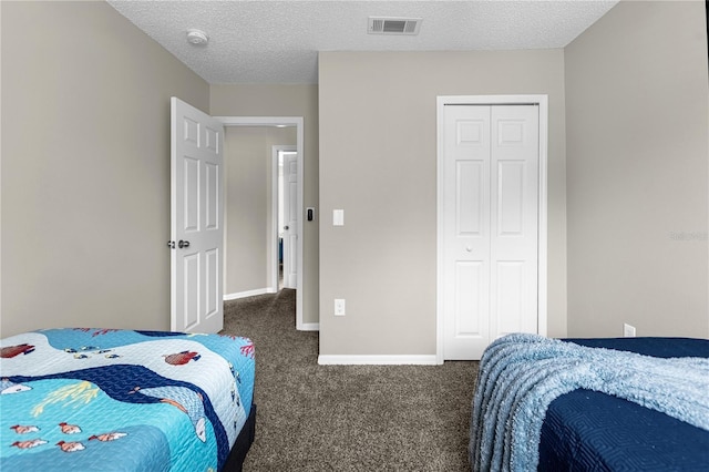 bedroom with a textured ceiling, dark carpet, and a closet