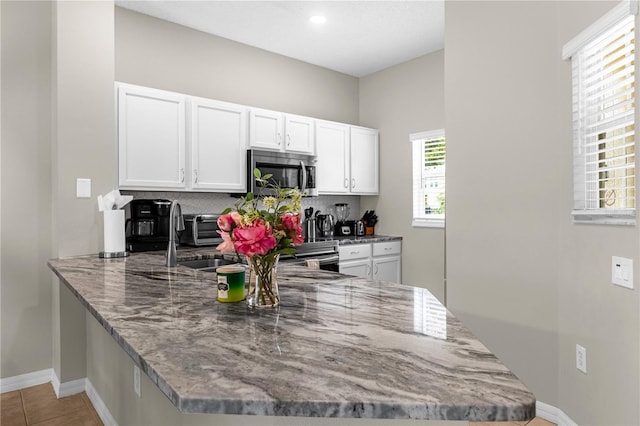 kitchen with kitchen peninsula, tile patterned flooring, white cabinets, and backsplash