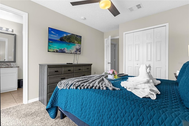 carpeted bedroom featuring ceiling fan, a closet, ensuite bathroom, and a textured ceiling