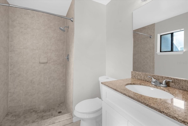 bathroom with toilet, vanity, a tile shower, and tile patterned flooring