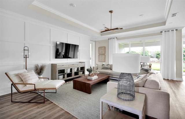 living room with a chandelier, light hardwood / wood-style flooring, a raised ceiling, and ornamental molding