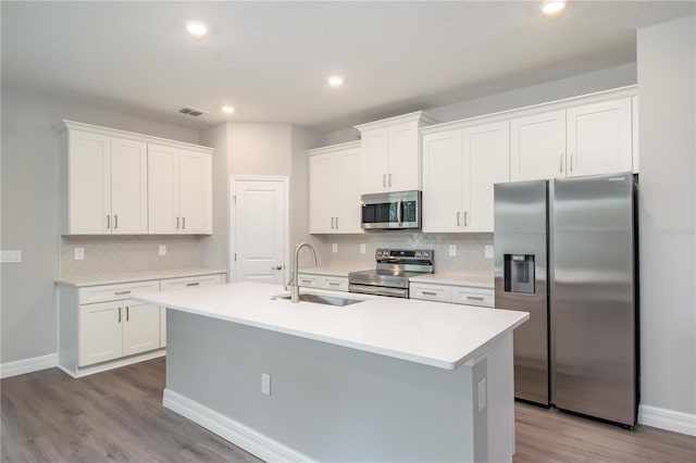 kitchen featuring a sink, white cabinets, light countertops, appliances with stainless steel finishes, and an island with sink