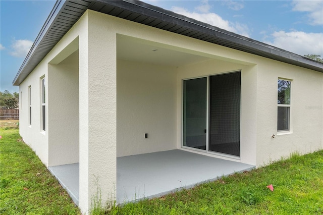 view of side of home featuring a patio area, a lawn, and stucco siding