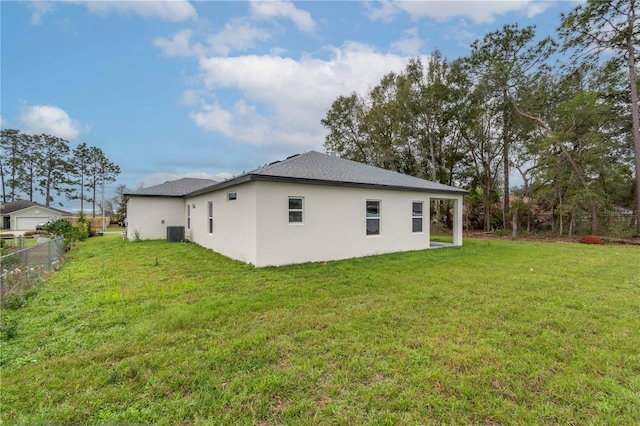 rear view of house with central air condition unit, stucco siding, fence, and a yard