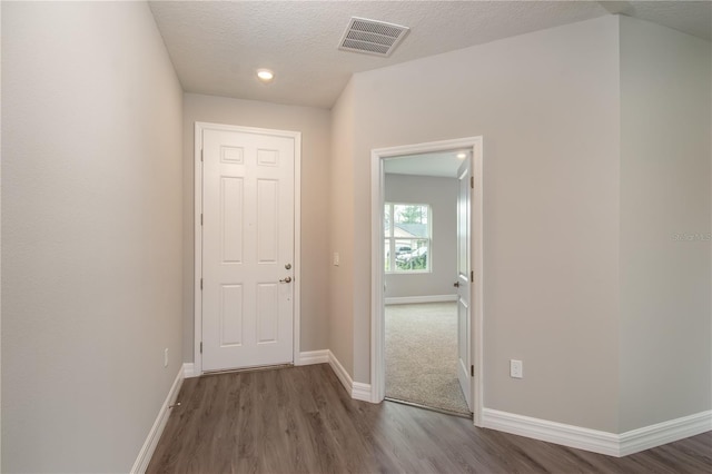 hall featuring baseboards, a textured ceiling, visible vents, and wood finished floors