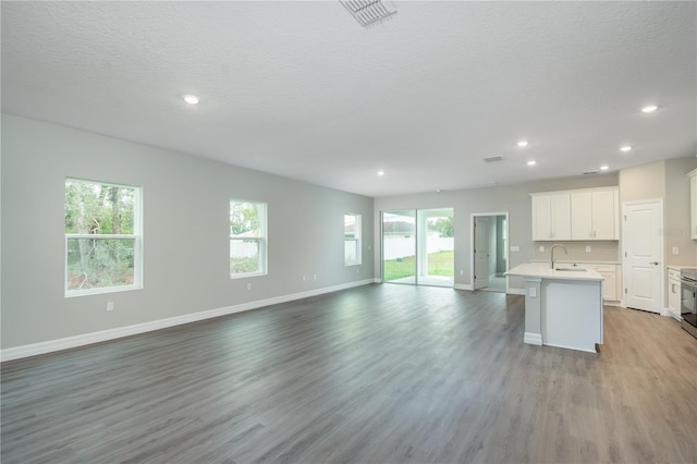 interior space with white cabinets, light wood-style flooring, open floor plan, a kitchen island with sink, and light countertops