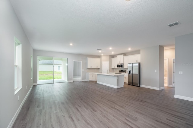 kitchen with white cabinets, an island with sink, appliances with stainless steel finishes, open floor plan, and light countertops