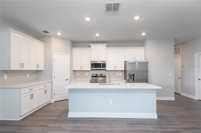 kitchen with visible vents, appliances with stainless steel finishes, a kitchen island with sink, white cabinets, and a sink