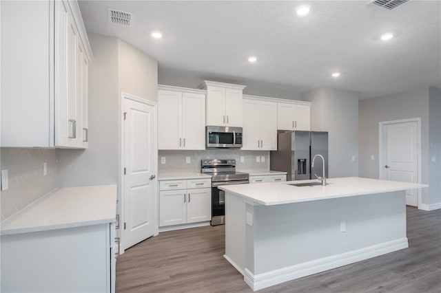 kitchen with a center island with sink, visible vents, white cabinets, stainless steel appliances, and light countertops