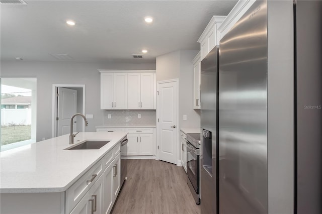 kitchen featuring light wood-style flooring, a sink, white cabinetry, appliances with stainless steel finishes, and decorative backsplash