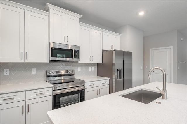 kitchen with white cabinets, light stone counters, appliances with stainless steel finishes, a sink, and backsplash