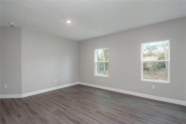 empty room featuring dark wood-type flooring, a textured ceiling, and baseboards