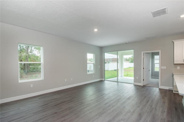 unfurnished living room featuring dark wood-style floors, a textured ceiling, visible vents, and baseboards