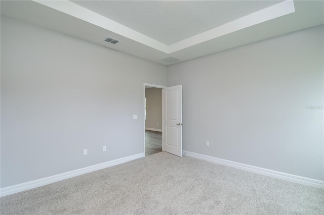 unfurnished room featuring carpet floors, a tray ceiling, visible vents, and baseboards