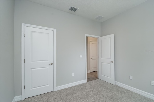 unfurnished bedroom with visible vents, light carpet, baseboards, and a textured ceiling