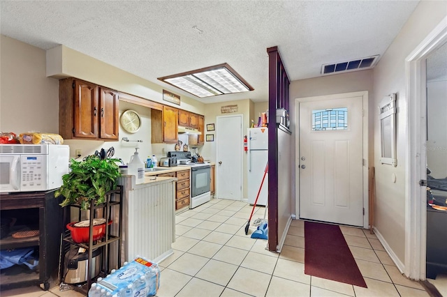 kitchen with a textured ceiling, white appliances, and light tile patterned flooring