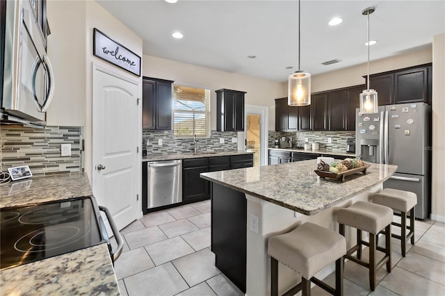 kitchen featuring a center island, stainless steel appliances, pendant lighting, decorative backsplash, and light tile patterned floors