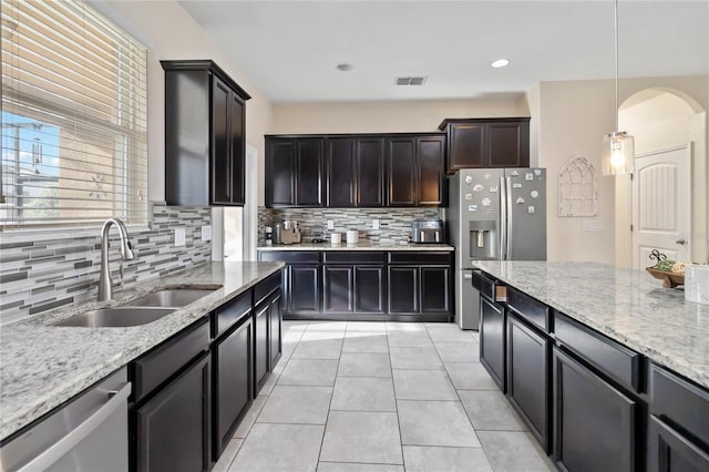 kitchen featuring sink, tasteful backsplash, light stone counters, decorative light fixtures, and appliances with stainless steel finishes