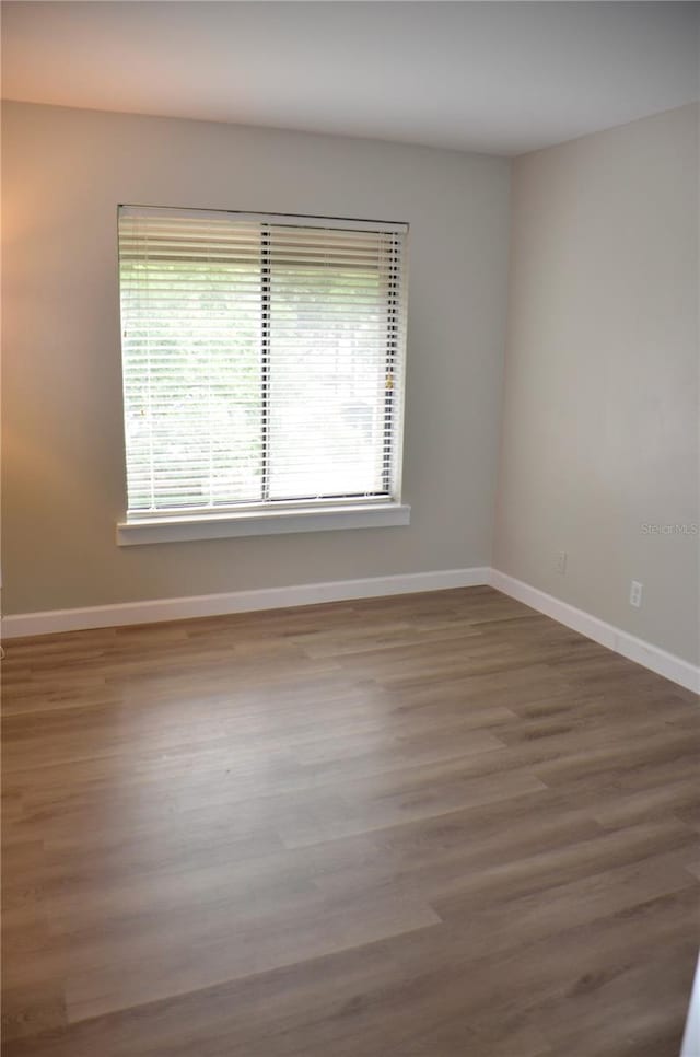 spare room with baseboards and dark wood-type flooring