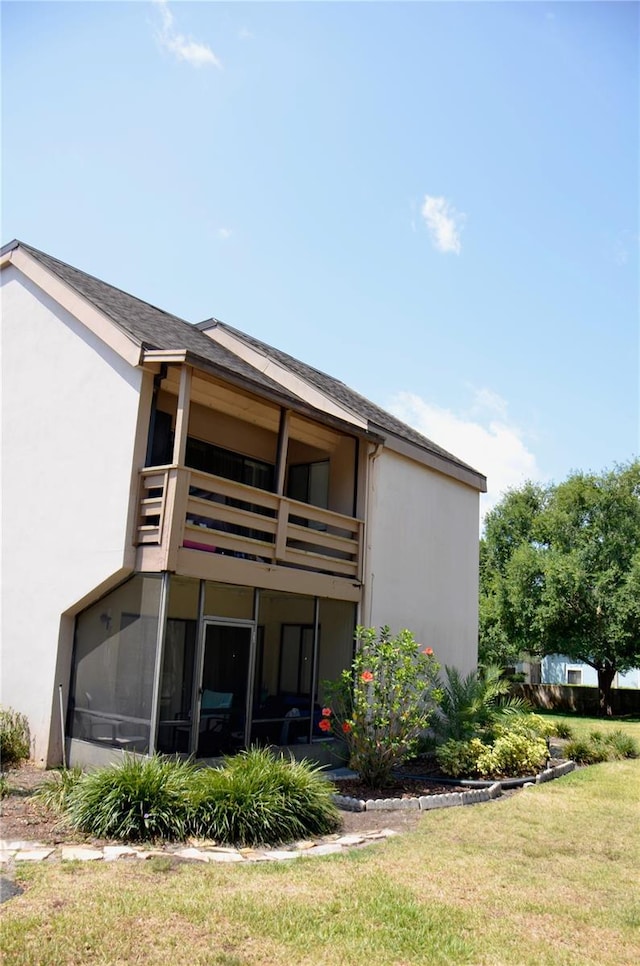 back of property featuring a yard, a balcony, and stucco siding