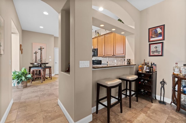 kitchen featuring decorative backsplash, a breakfast bar area, and black appliances