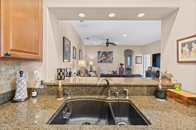 kitchen with tasteful backsplash, light stone counters, ceiling fan, and sink