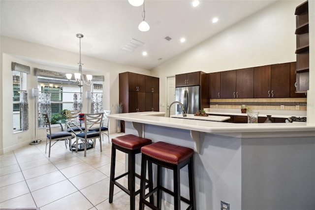 kitchen with hanging light fixtures, an inviting chandelier, tasteful backsplash, stainless steel fridge, and dark brown cabinets