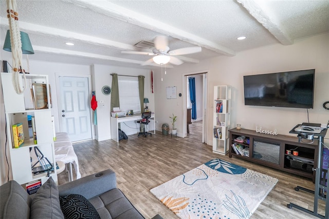 living room featuring hardwood / wood-style flooring, ceiling fan, beam ceiling, and a textured ceiling