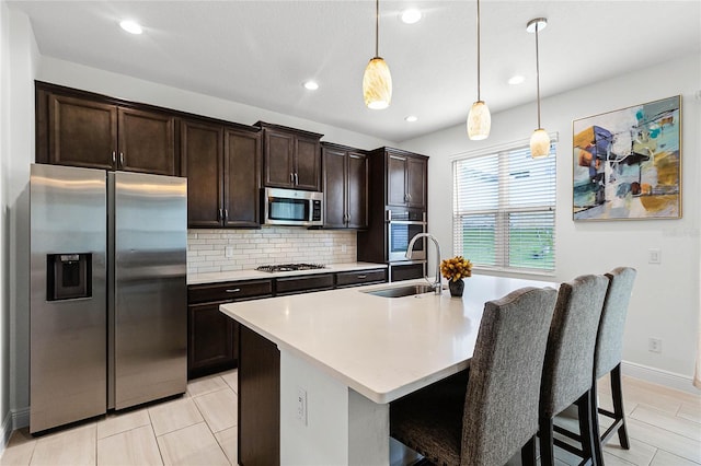 kitchen featuring tasteful backsplash, dark brown cabinetry, stainless steel appliances, hanging light fixtures, and an island with sink