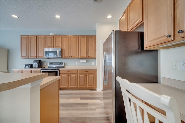 kitchen with light wood-type flooring, light brown cabinets, a textured ceiling, and appliances with stainless steel finishes