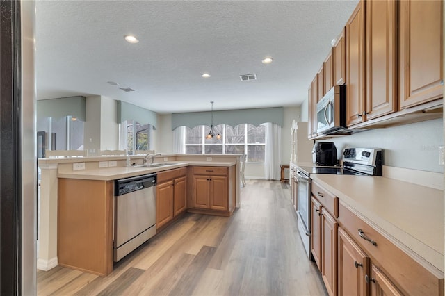 kitchen with sink, hanging light fixtures, stainless steel appliances, a textured ceiling, and light wood-type flooring