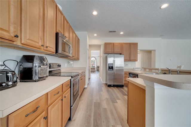 kitchen featuring sink, a textured ceiling, light brown cabinets, stainless steel appliances, and light hardwood / wood-style floors