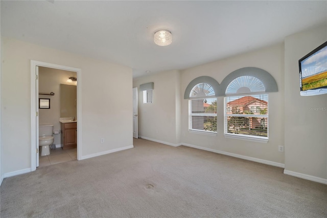 unfurnished bedroom featuring light carpet, multiple windows, and ensuite bathroom