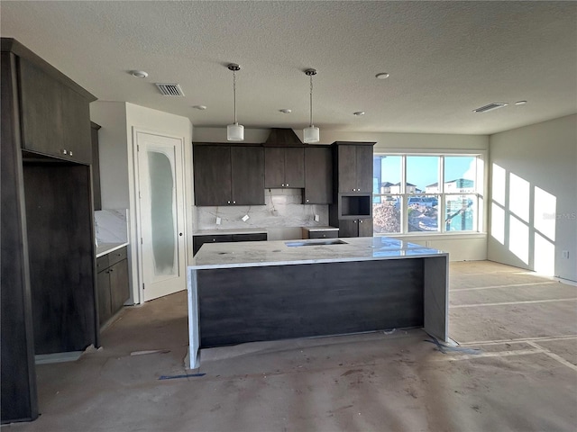 kitchen with decorative backsplash, a textured ceiling, dark brown cabinetry, a center island, and hanging light fixtures