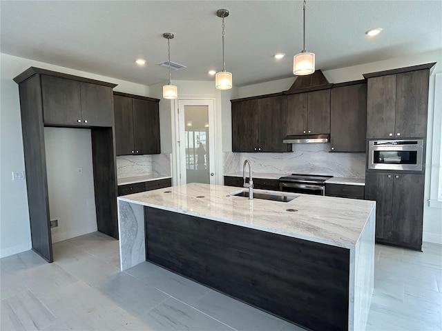 kitchen with sink, decorative light fixtures, an island with sink, stainless steel appliances, and light stone countertops