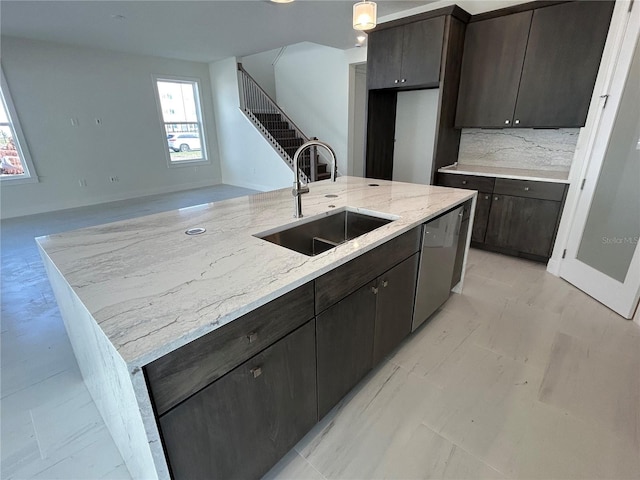 kitchen featuring an island with sink, sink, decorative backsplash, stainless steel dishwasher, and light stone countertops