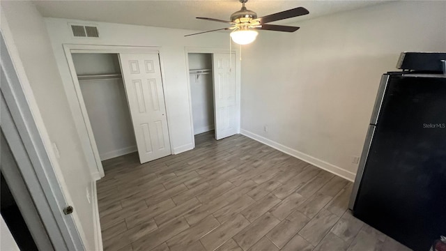 unfurnished bedroom with ceiling fan, two closets, stainless steel refrigerator, and light hardwood / wood-style flooring