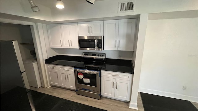 5587 Devonbriar Way Unit 104, Orlando, FL 32822 - kitchen featuring appliances with stainless steel finishes, dark countertops, white cabinets, and light wood-style floors