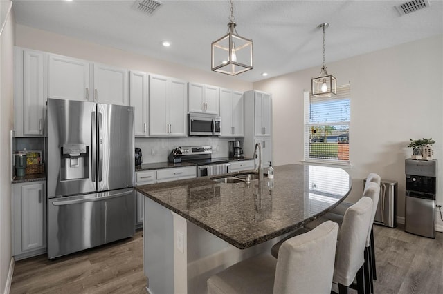 kitchen featuring pendant lighting, a center island with sink, sink, white cabinetry, and stainless steel appliances