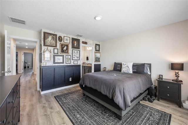 bedroom featuring ensuite bathroom, light hardwood / wood-style floors, and a textured ceiling