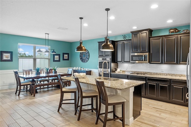 kitchen with appliances with stainless steel finishes, decorative light fixtures, an island with sink, a breakfast bar area, and decorative backsplash