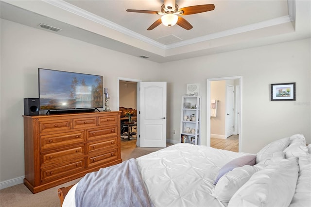 carpeted bedroom featuring crown molding, a tray ceiling, ensuite bath, and ceiling fan