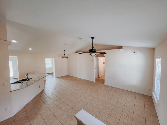 unfurnished living room featuring vaulted ceiling, sink, light tile patterned floors, and ceiling fan with notable chandelier