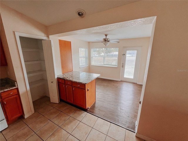 kitchen with ceiling fan, light tile patterned flooring, light stone countertops, and kitchen peninsula