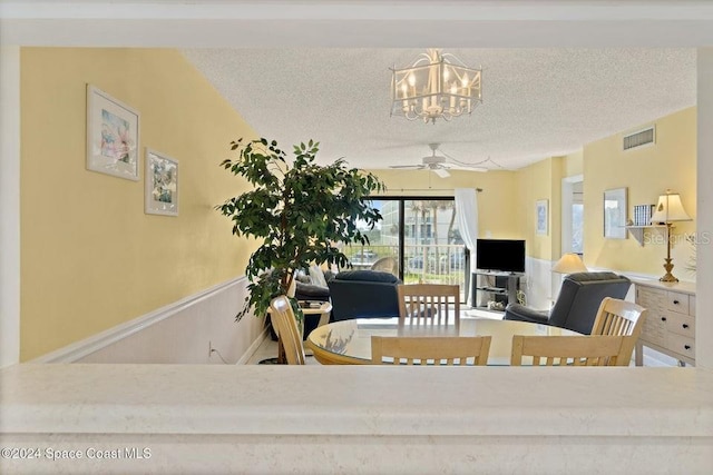 dining area featuring ceiling fan with notable chandelier and a textured ceiling