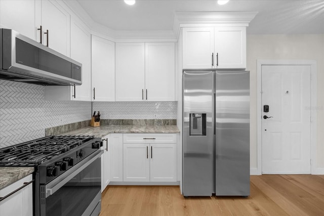 kitchen featuring light stone countertops, stainless steel appliances, backsplash, light hardwood / wood-style floors, and white cabinets