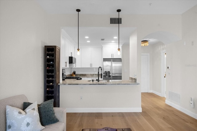 kitchen with pendant lighting, built in fridge, sink, light stone counters, and white cabinetry