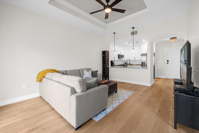 living room featuring sink, crown molding, light hardwood / wood-style flooring, ceiling fan, and a tray ceiling