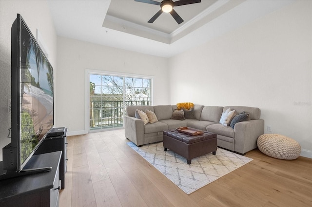 living room with ceiling fan, light hardwood / wood-style floors, ornamental molding, and a tray ceiling